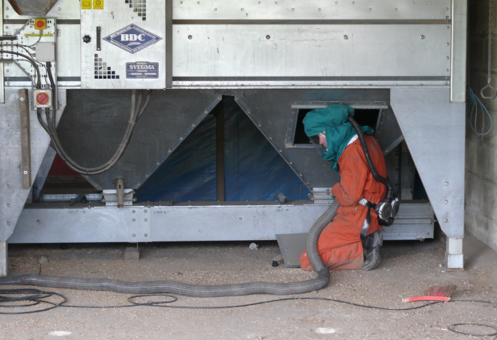 Person in orange hazmat suit cleaning grain machinery